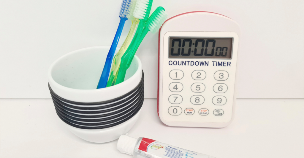 Toothbrushes in cup next to toothpaste and timer.