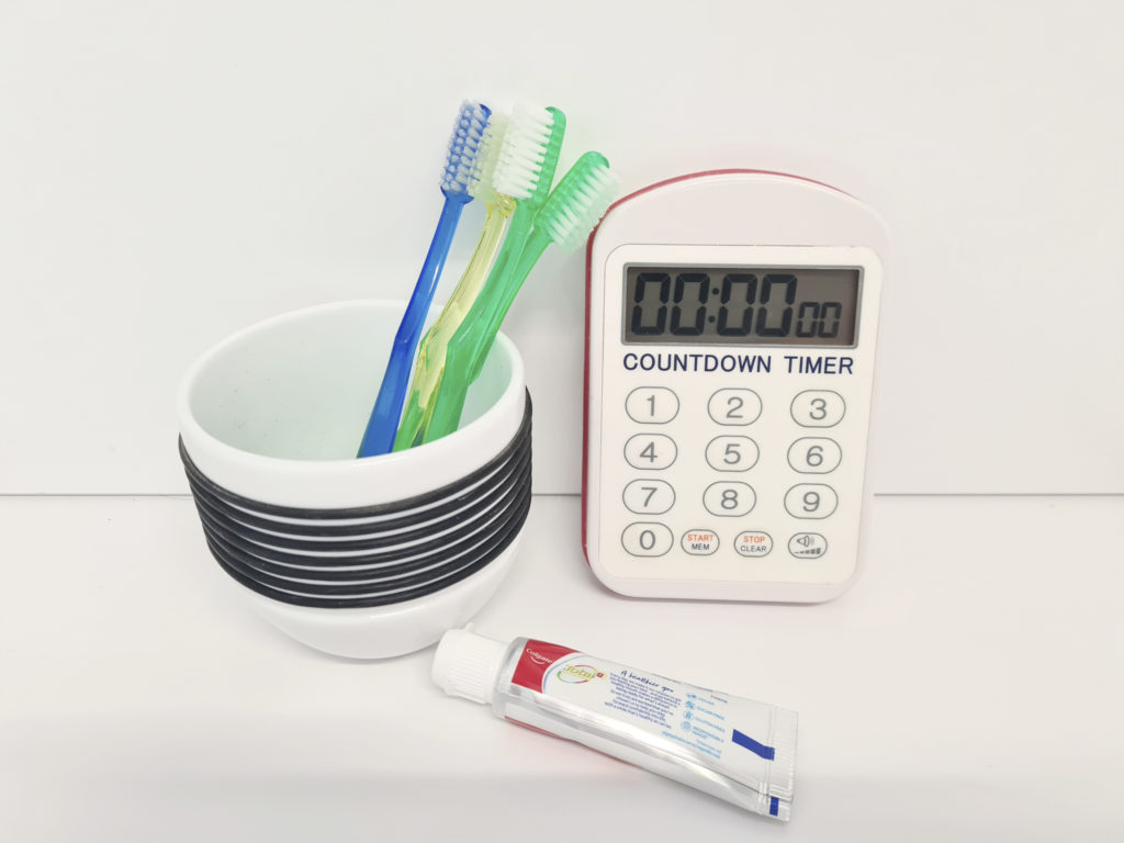 A clock and tube of toothpaste beside tooth brushes.