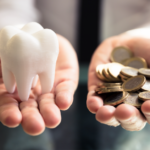 Close-up of a person's hand holding white tooth and coins