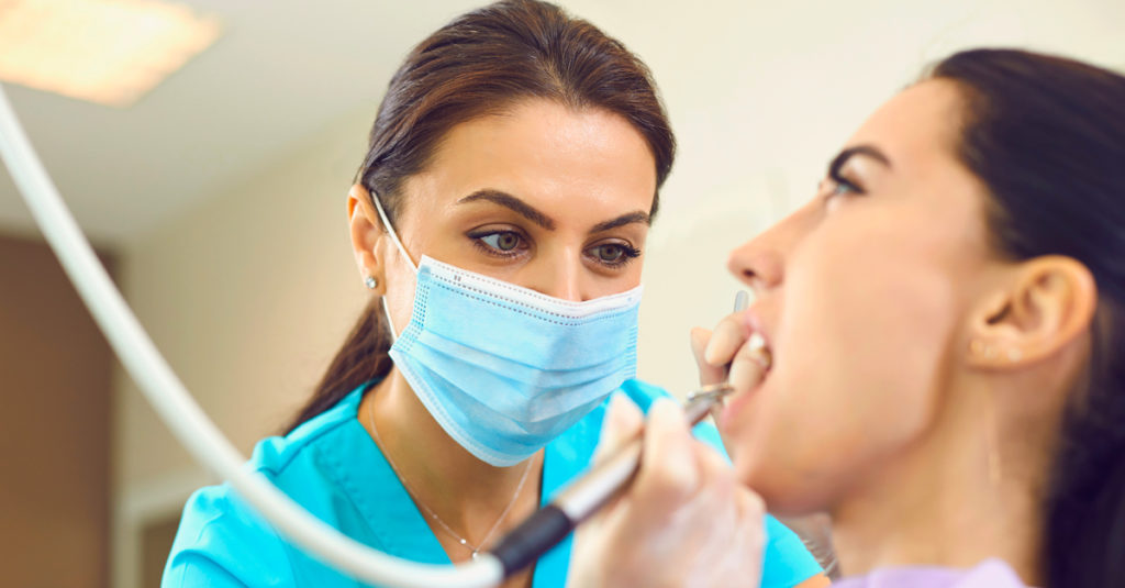 Concentrated female specialist removing tooth stone from client's teeth using ultrasonic scaler.
