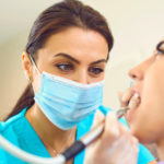 Concentrated female specialist removing tooth stone from client's teeth using ultrasonic scaler.