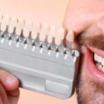Young man with teeth color samples on beige background.