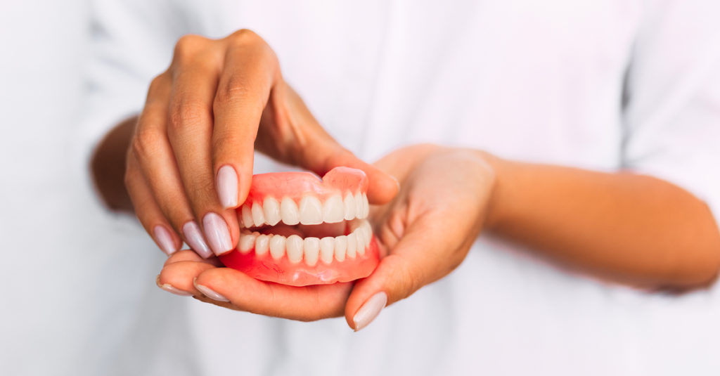 The dentist is holding a close-up of a dental prosthesis in the hands in her hands.