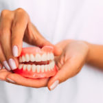 The dentist is holding a close-up of a dental prosthesis in the hands in her hands.