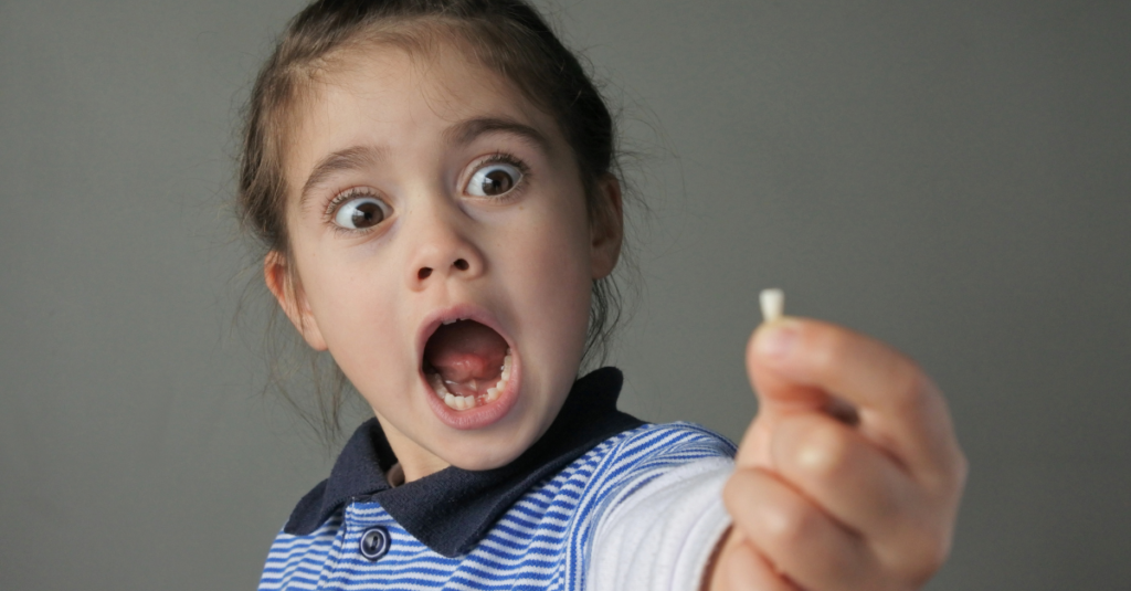Young girl (female age 6) surprised to find that she have lost her first bottom front milk teeth isolated on grey background.