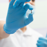 Dentist in a white uniform with blue latex gloves holding a dental implant.