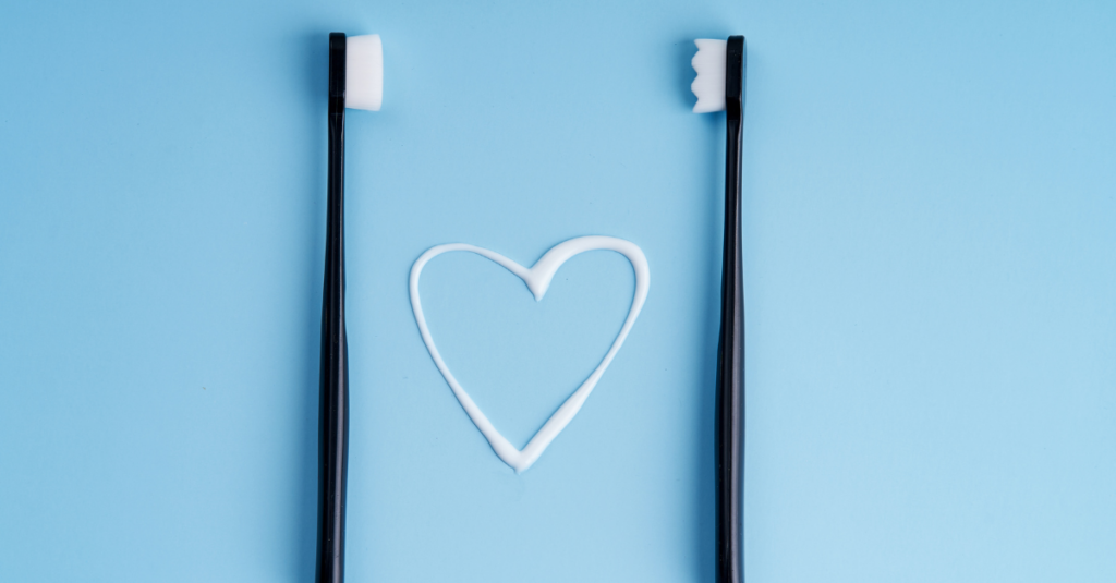 Two black toothbrushes with white toothpaste in the shape of a heart.