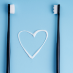 Two black toothbrushes with white toothpaste in the shape of a heart.