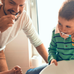 Dad and kids brushing teeth over sink.