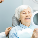 Happy elderly woman enjoying her smile looking to the mirror in the dental office.