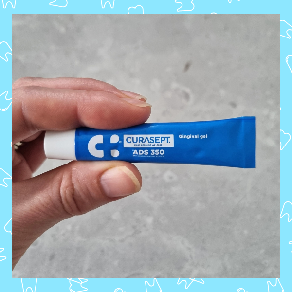 Hand holding a small blue tube of Curasept gingival gel.