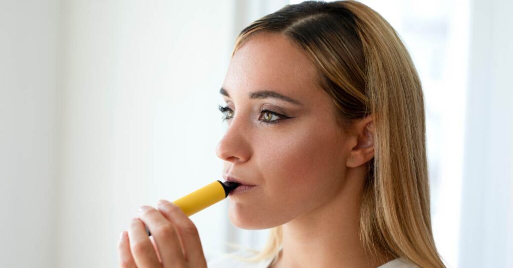Woman holding a yellow e-cigarette to lips.