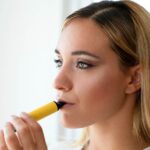 Woman holding a yellow e-cigarette to lips.