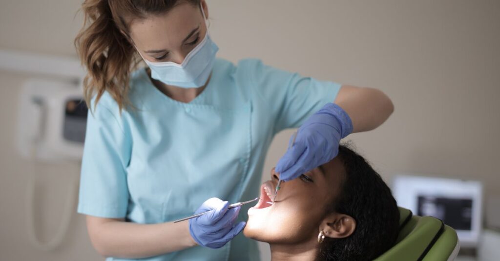 oral health therapist using dental tools to look into a patient's mouth