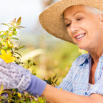 Happy senior woman with dental implants in hat gardening.