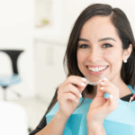 person at a dental office holding up clear aligners to her mouth