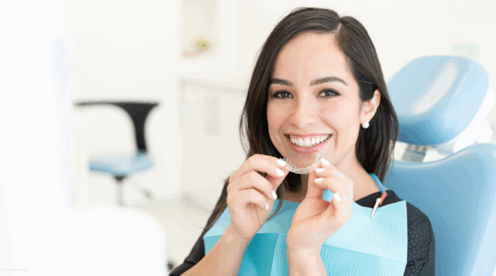 person at a dental office holding up clear aligners to her mouth