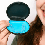 Close-up of smiling woman holding a case with a clear aligner inside.
